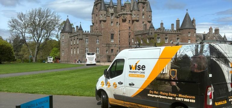 A Wise Property Care service van parked outside a historic castle with multiple turrets under a partly cloudy blue sky. A sign in the foreground reads "Castle & Visitor Reception."